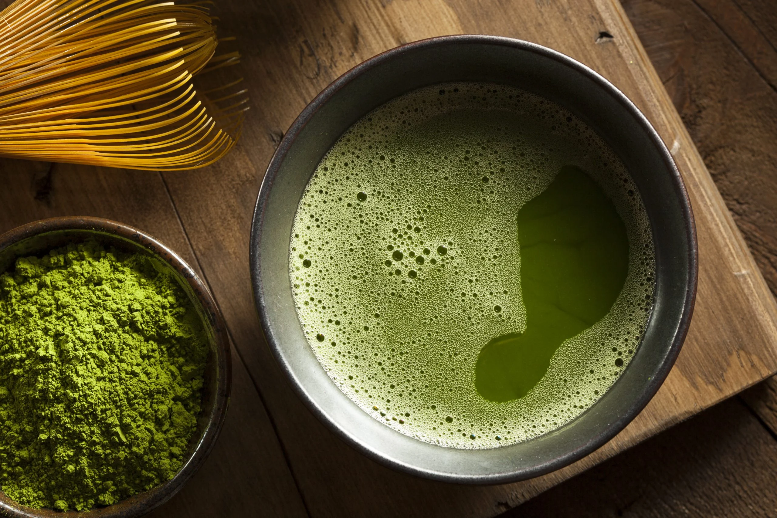 Brewed matcha next to powder and chasen.
